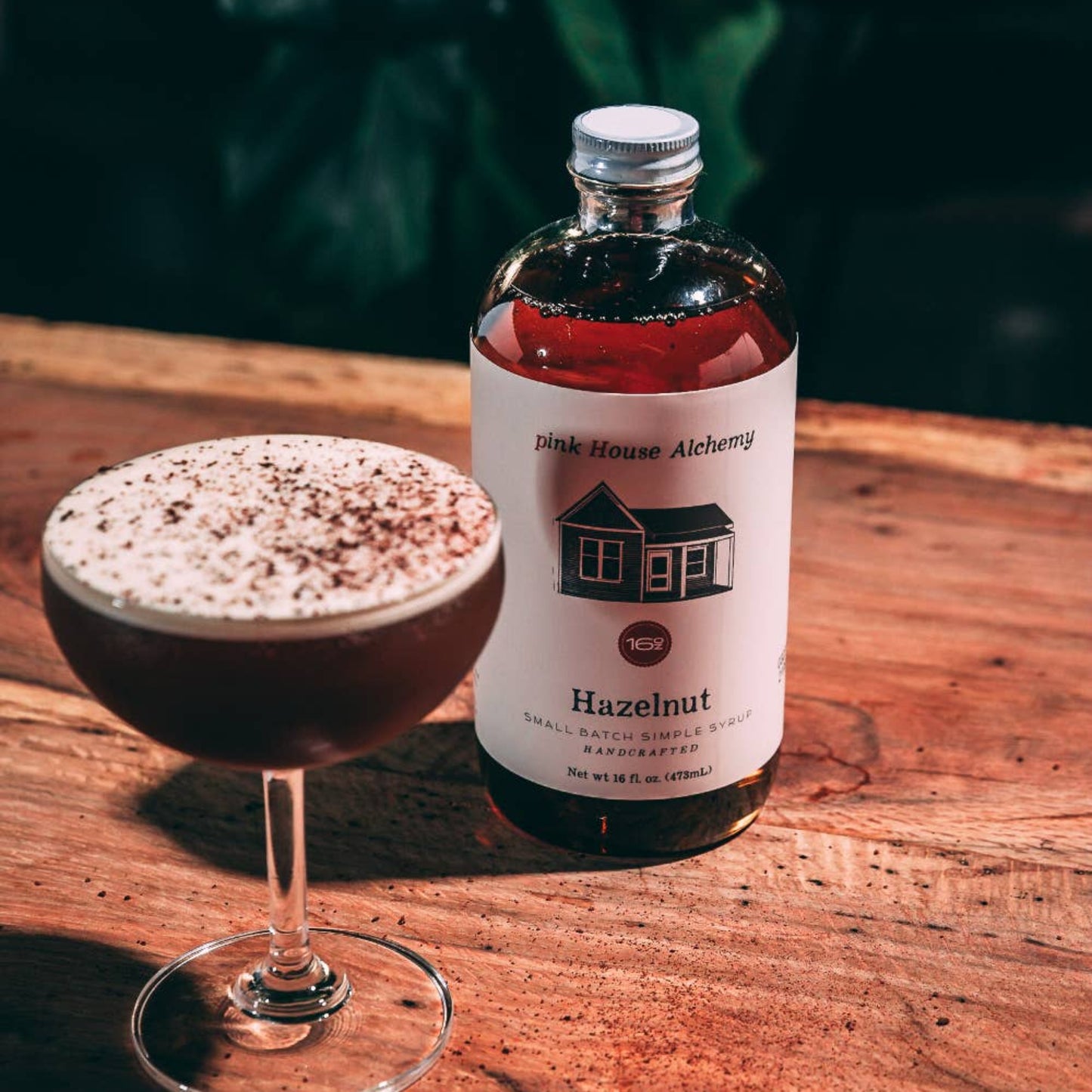 Bottle of hazelnut syrup next to a glass of coffee on a wooden surface