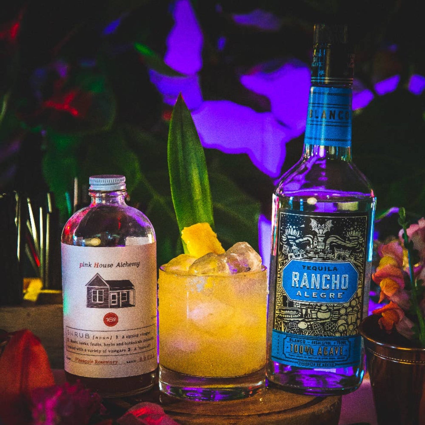 Two bottles of alcohol, a cocktail with ice and a lemon wedge, on a dark background.